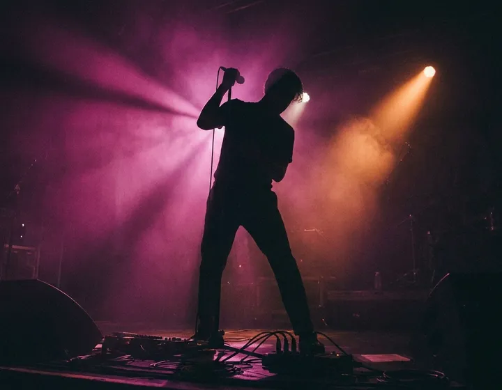 Silhouette of an artist performing live on stage under purple and orange lights