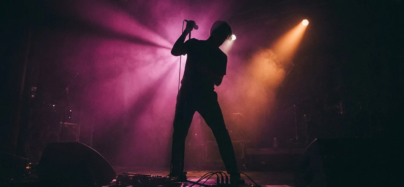 Silhouette of an artist performing live on stage under purple and orange lights